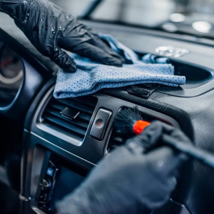 Detailer cleaning a car dashboard and vents during an interior detail
